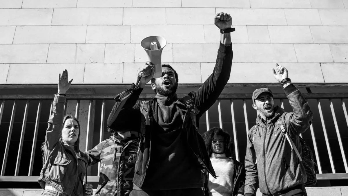 Black and White Photo of a Group of Protestors with a Black Man in the Middle Leading the Group with a Megaphone and His Fist in the Air for an Essay on the Importance of Sociology in Our Society